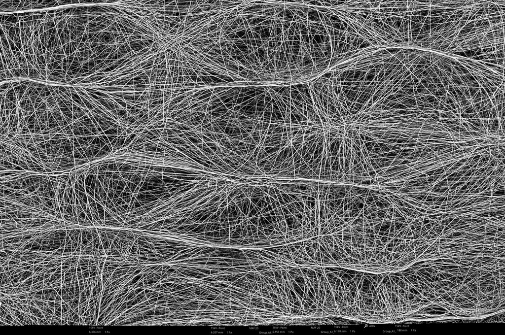 Stitched image of 40 scanning electron micrographs of polycaprolactone (PCL) fibers collected on top of a 1 cm diameter rod at 200 rpm and with the collector grounded in a Fluidnatek LE-100 equipment. At 0 kV on the collector a rough microstructural surface is observed due to residual charge, causing fibers to localize in certain areas of the sample, affecting the final porosity of the electrospun material. By using a higher bias this effect will be completely removed and the final sample will contain a smooth surface.